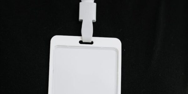 Plastic name tag with white ribbon and blank paper hanging on black background